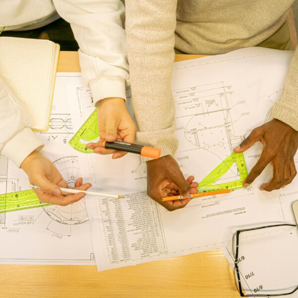 High angle view of architects working on blueprints, using rulers and markers on a wooden table.