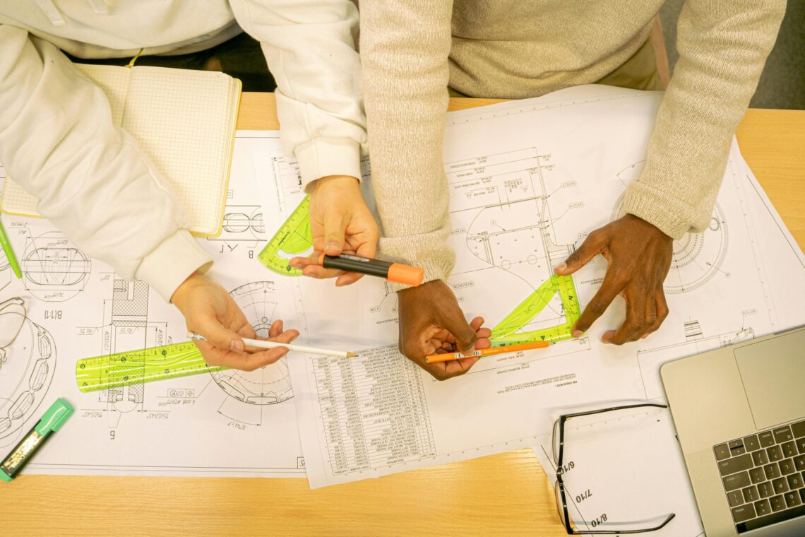 High angle view of architects working on blueprints, using rulers and markers on a wooden table.