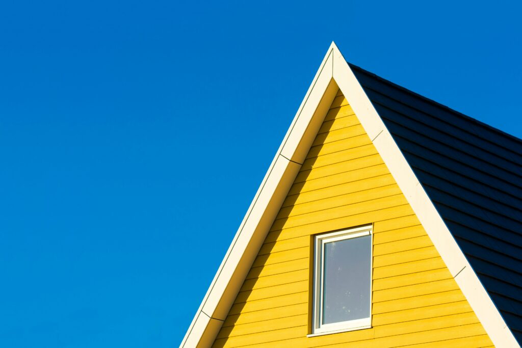 Close-up of a yellow house with a triangle roof against a clear blue sky.