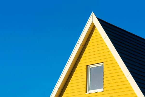 Close-up of a yellow house with a triangle roof against a clear blue sky.